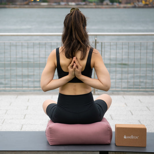 woman sitting on a rose indian cotton rectangular yoga bolster in a seated pose